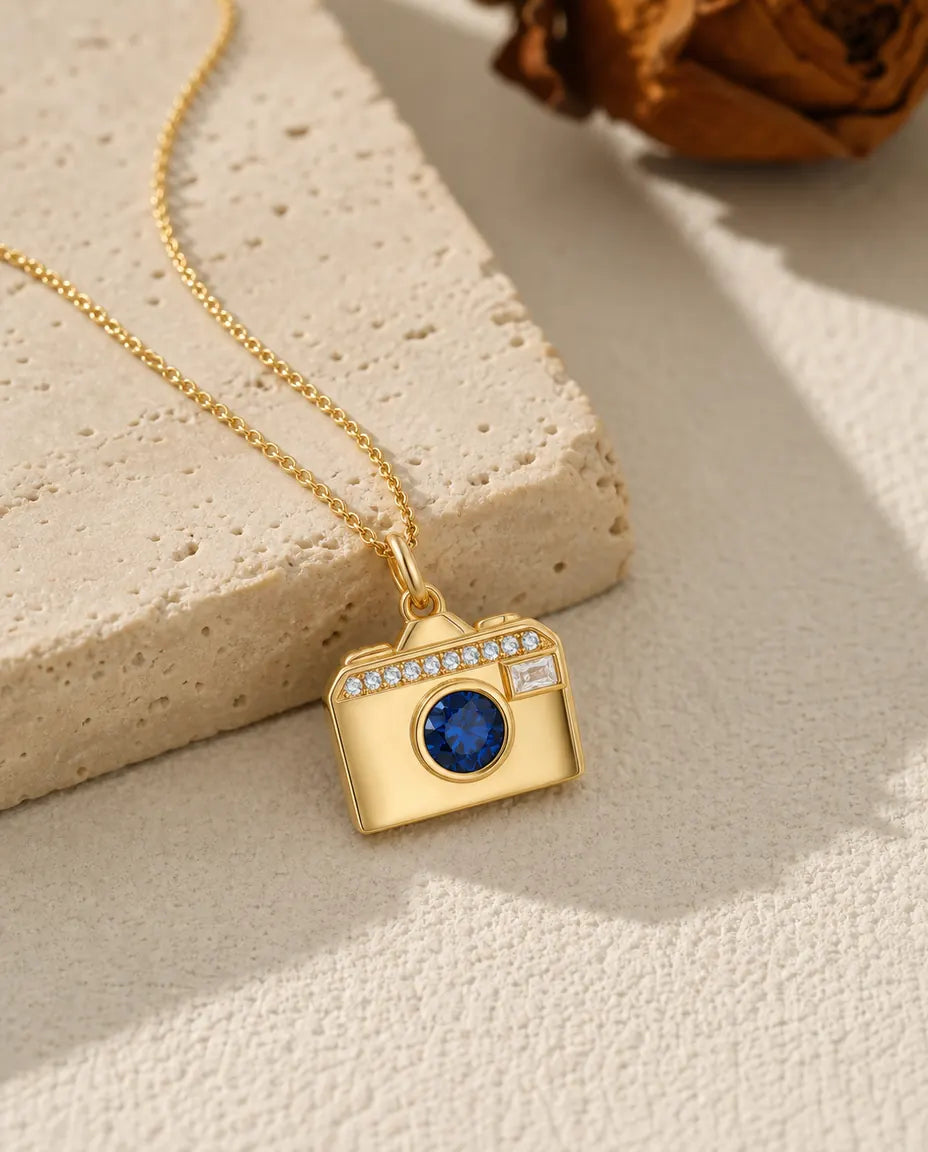 Gold camera photo locket necklace with a blue birthstone lens