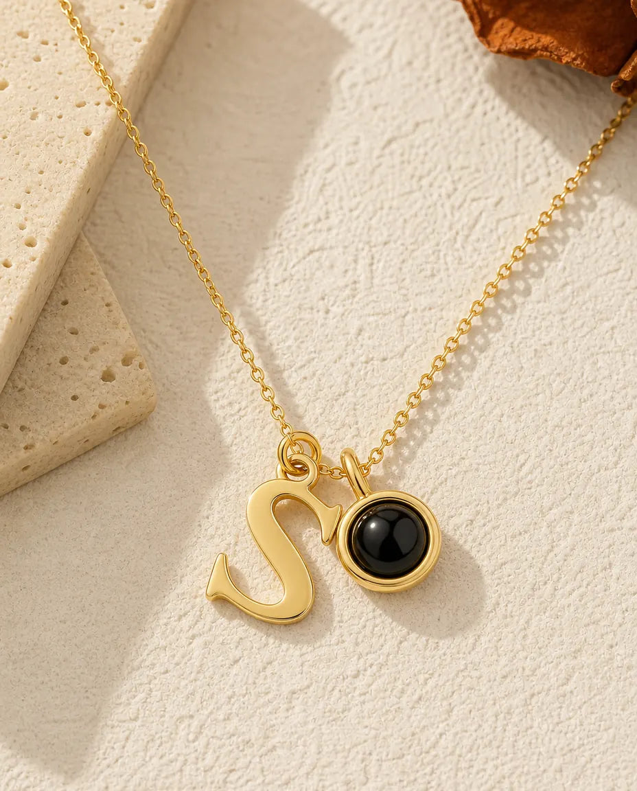 Gold initial photo projection necklace with a script letter charm and a black projection bead