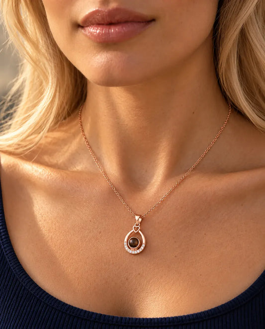 Woman in a navy top wearing the rose gold tone teardrop projection necklace