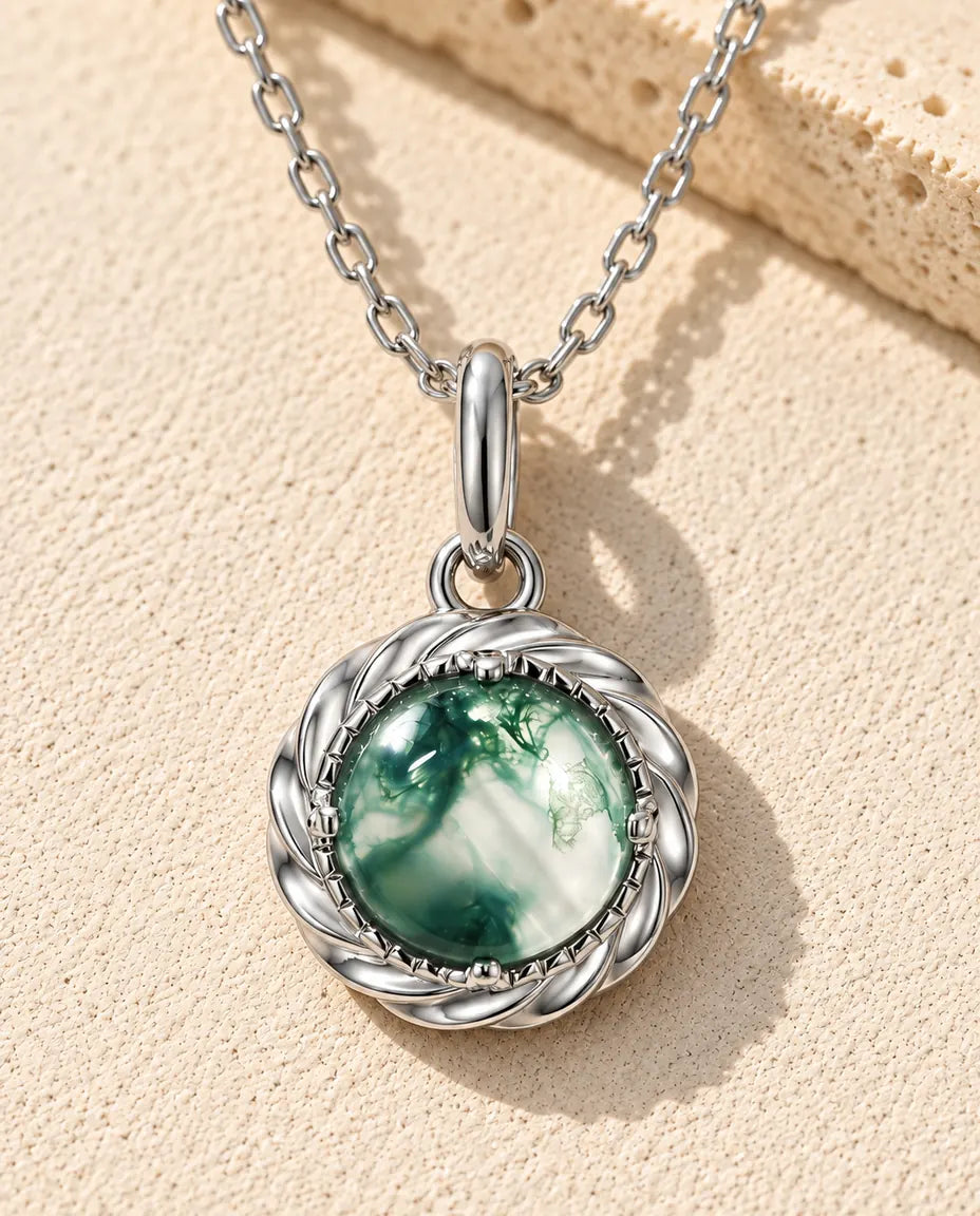 Round Moss Agate Pendant Necklace in 925 Sterling Silver - lying on a cream textured surface beside a travertine block