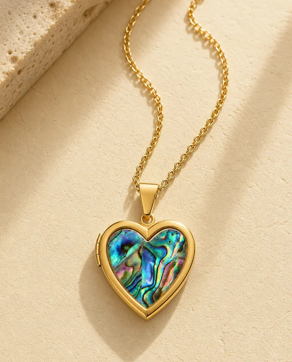 Gold heart locket necklace with iridescent abalone shell front on a warm cream stone surface