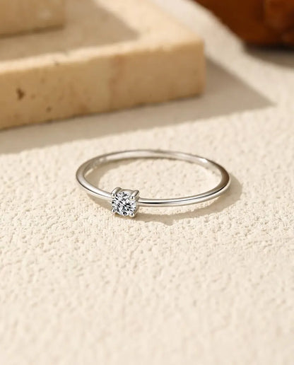 Dainty Moissanite Solitaire Ring in 925 Sterling Silver - lying flat on a cream textured surface