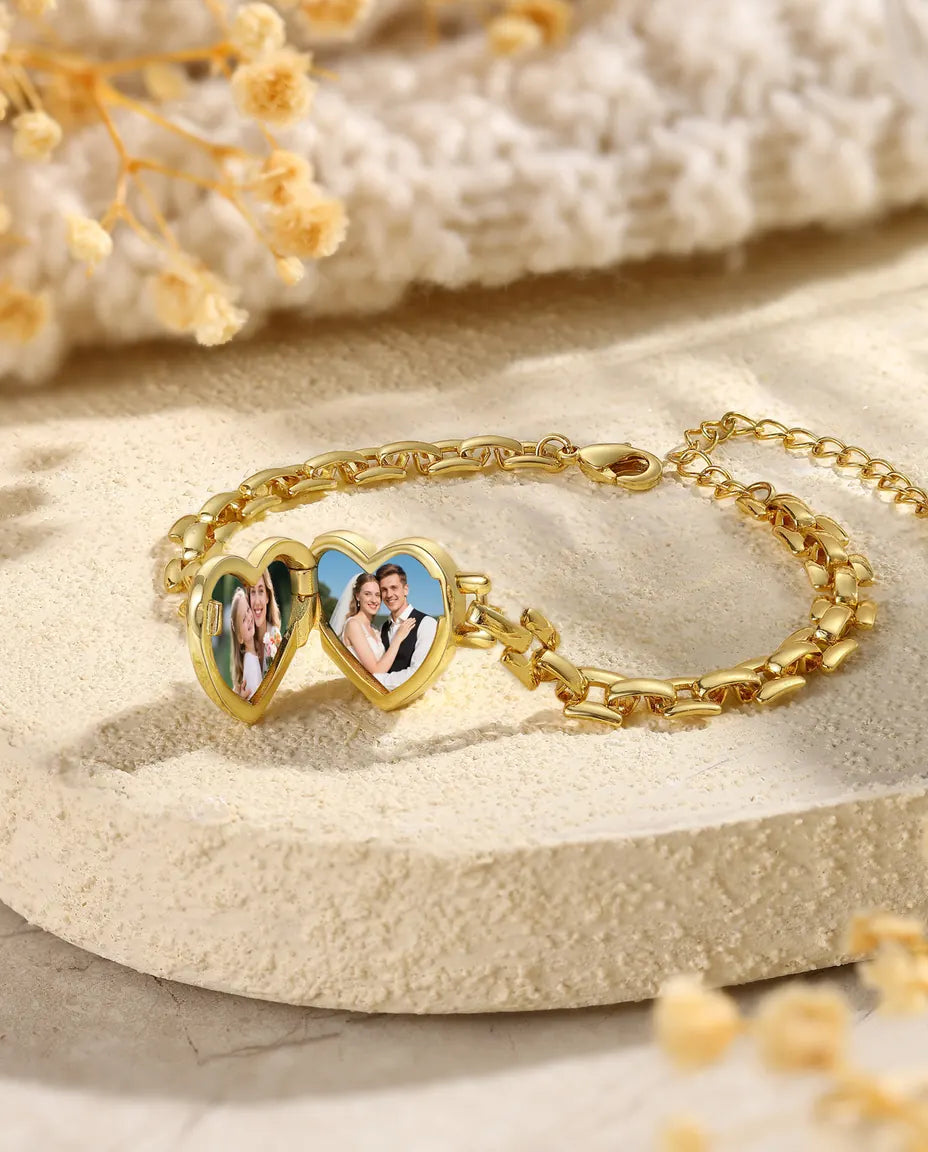 Gold heart locket bracelet lying open showing two photos on a watch band chain