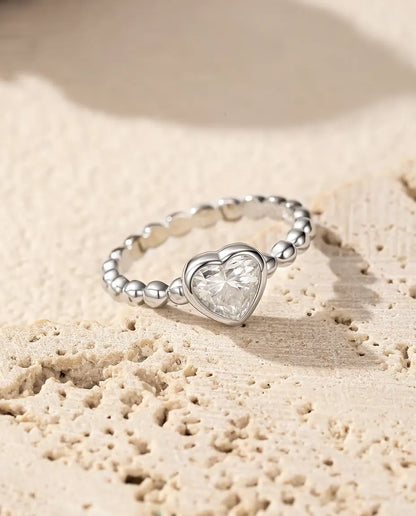 Heart Moissanite Ring in 925 Sterling Silver - resting on a porous travertine surface