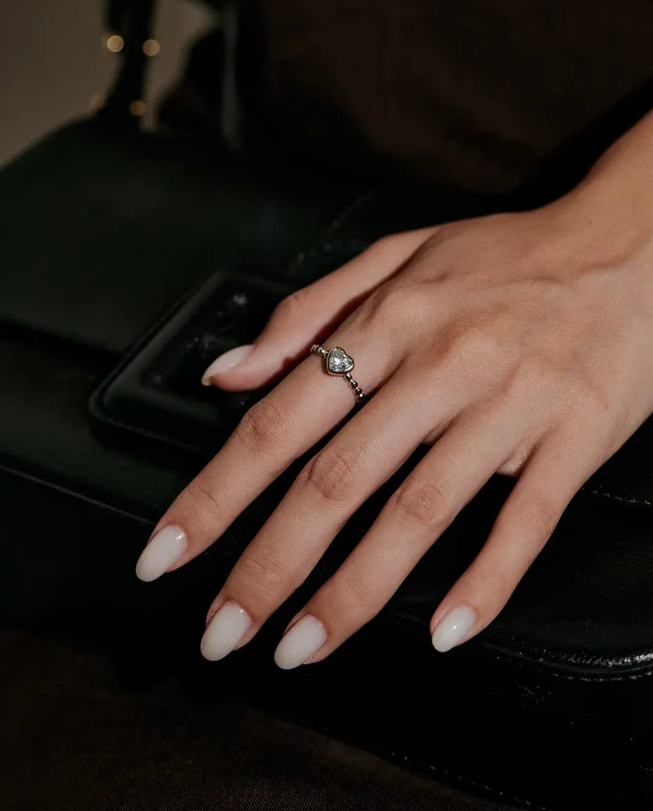 Heart Moissanite Ring in 925 Sterling Silver - worn on a hand resting on a black bag