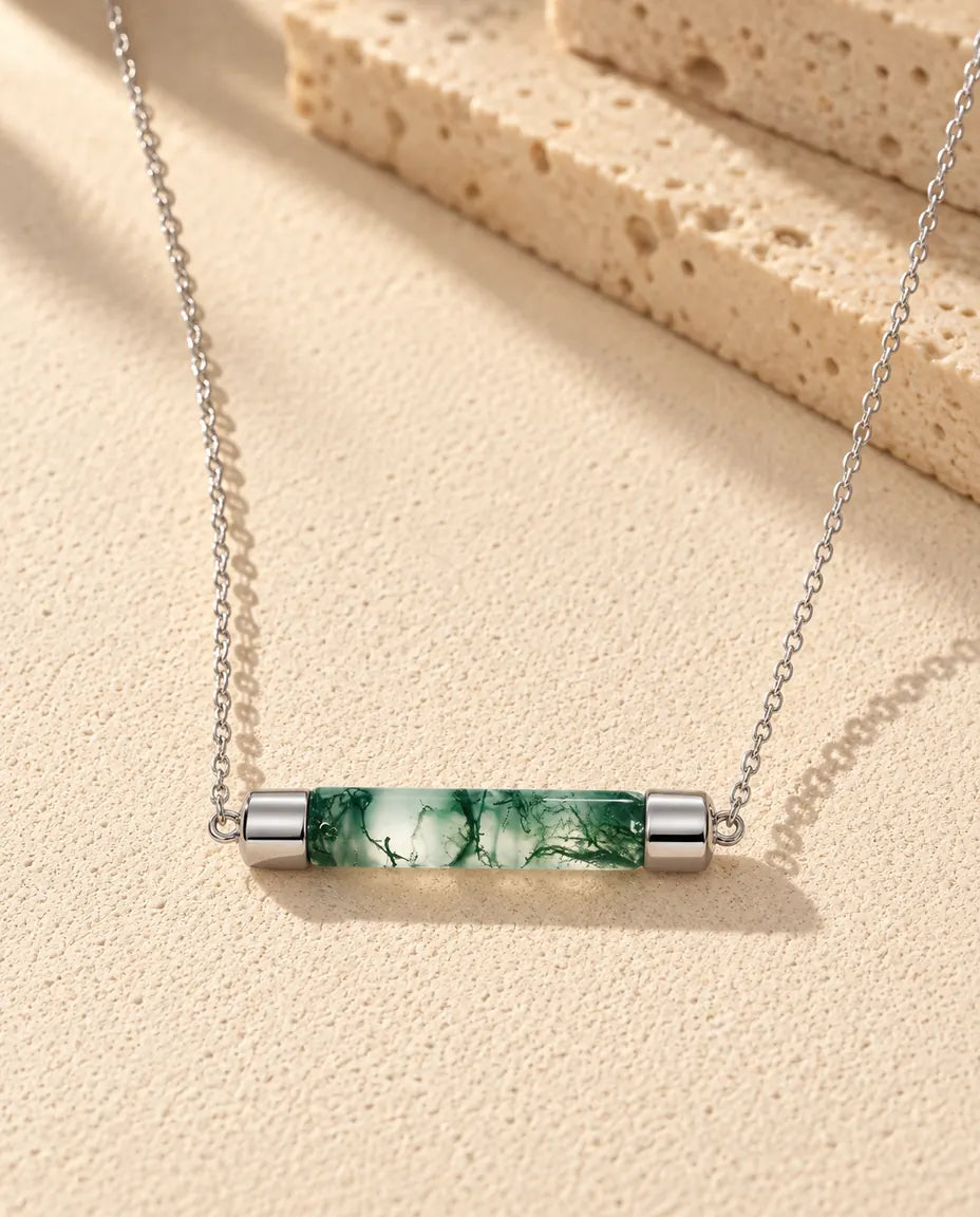 Moss Agate Bar Necklace in 925 Sterling Silver - lying on a cream textured surface beside a travertine block