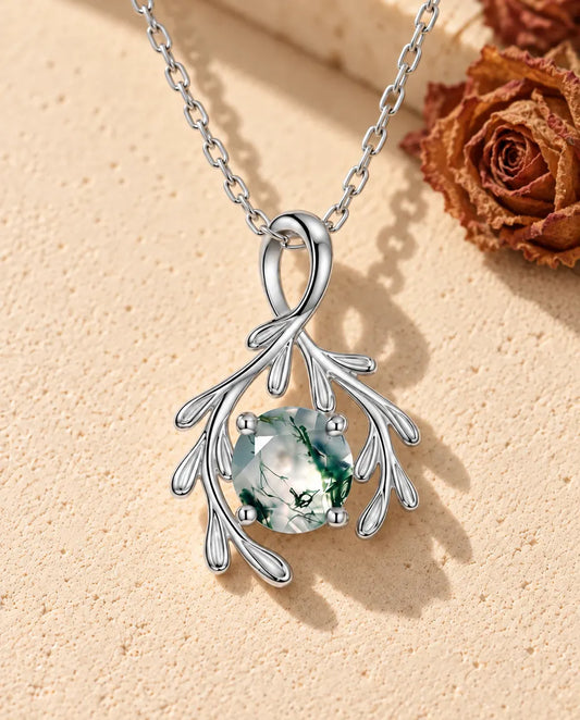 Moss Agate Branch Necklace in 925 Sterling Silver - lying on a cream textured surface beside a travertine block