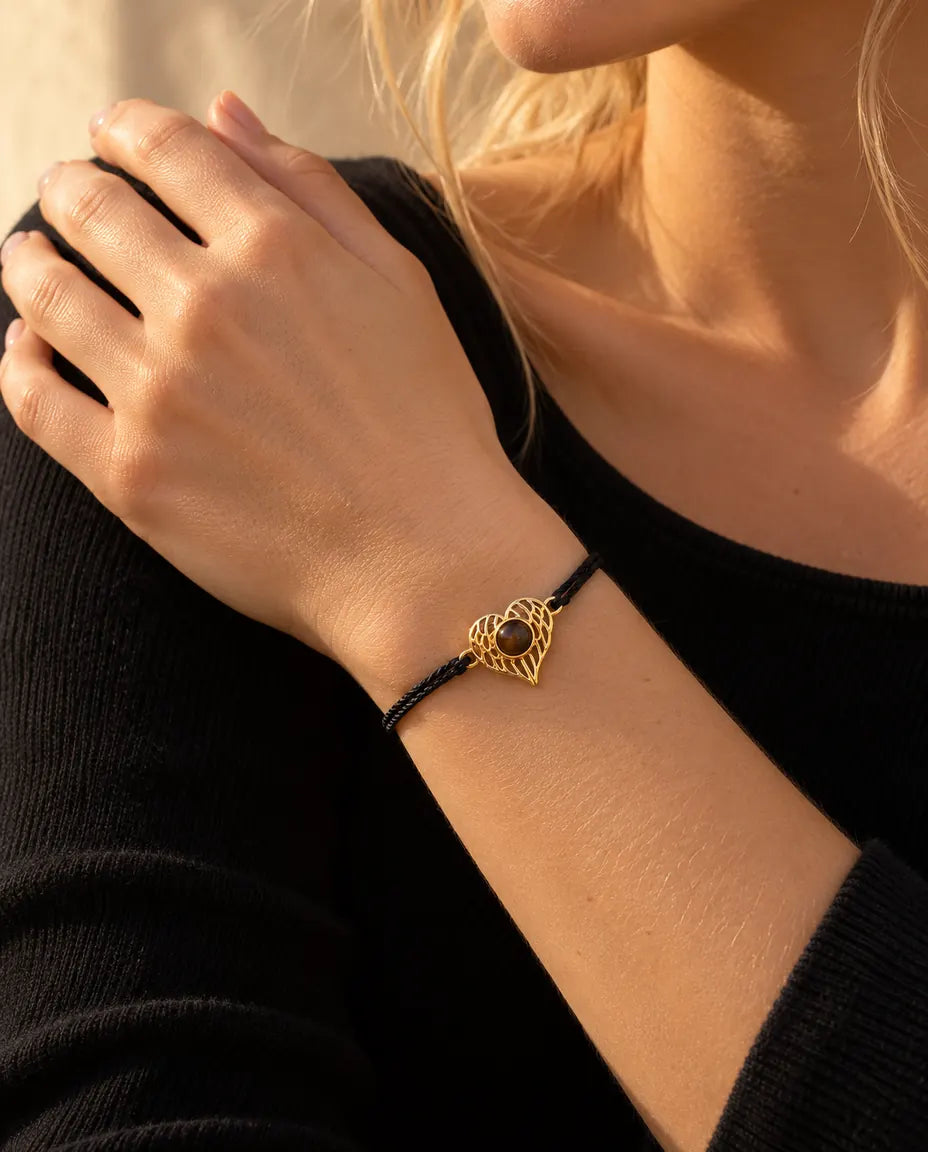 Close-up of the gold tone angel wing heart on a black rope cord, hand resting on the shoulder