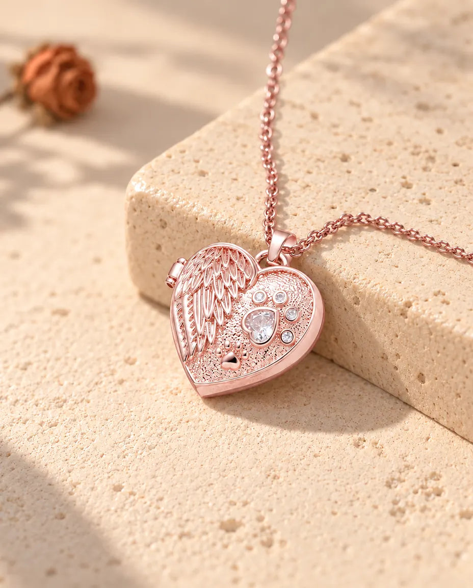 Rose gold tone angel wing paw print heart photo locket necklace on travertine in warm sunlight