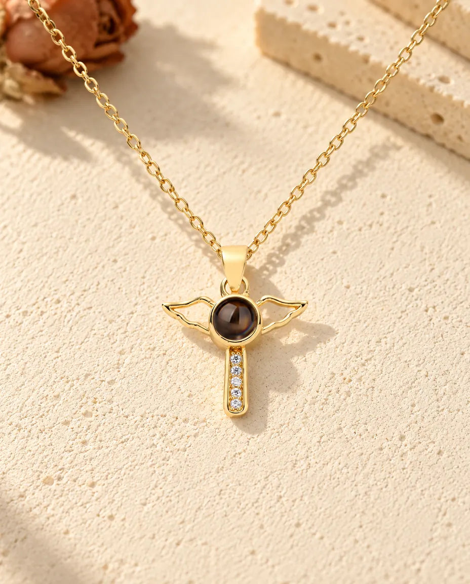 Front view of the gold tone cross with open angel wings and the projection stone at its center