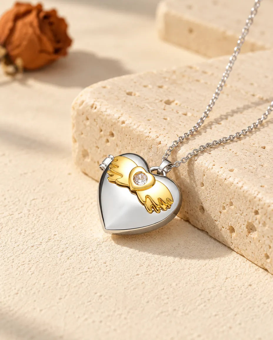 Personalized angel wings heart photo locket necklace in silver tone with gold tone angel wings, resting on a travertine block