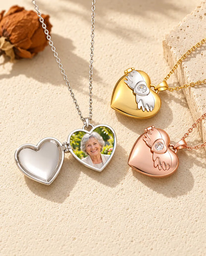 Silver tone angel wings heart photo locket opened to show a grandmother's portrait inside, beside closed gold tone and rose gold tone lockets