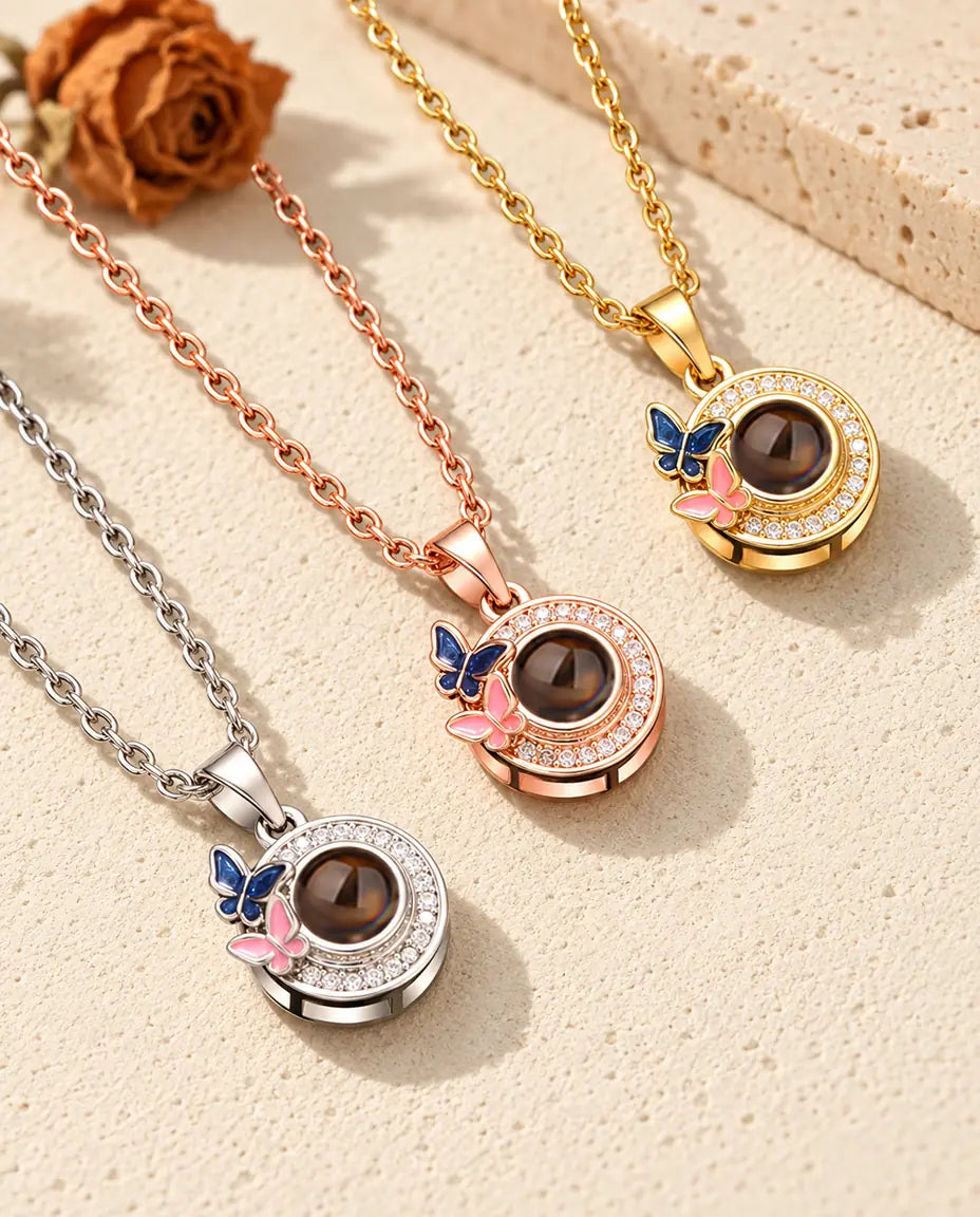 Three colors of the butterfly photo projection necklace on a diagonal on cream plaster
