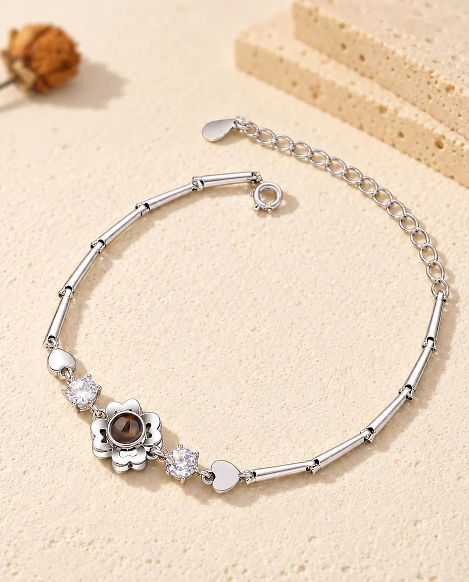 Personalized clover flower photo projection bracelet in silver tone on a slim bar chain, lying on cream plaster