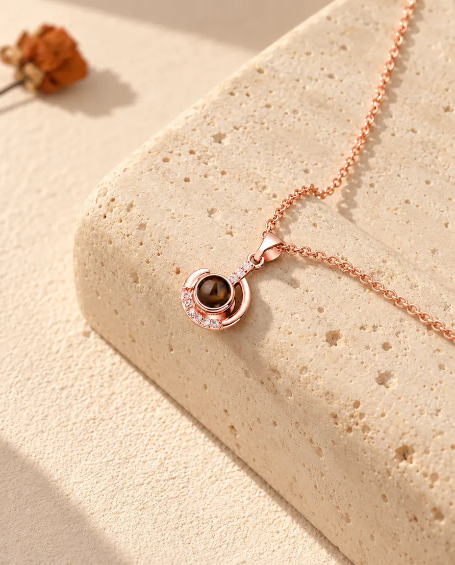 Personalized rose gold tone crescent moon photo projection necklace on a travertine block