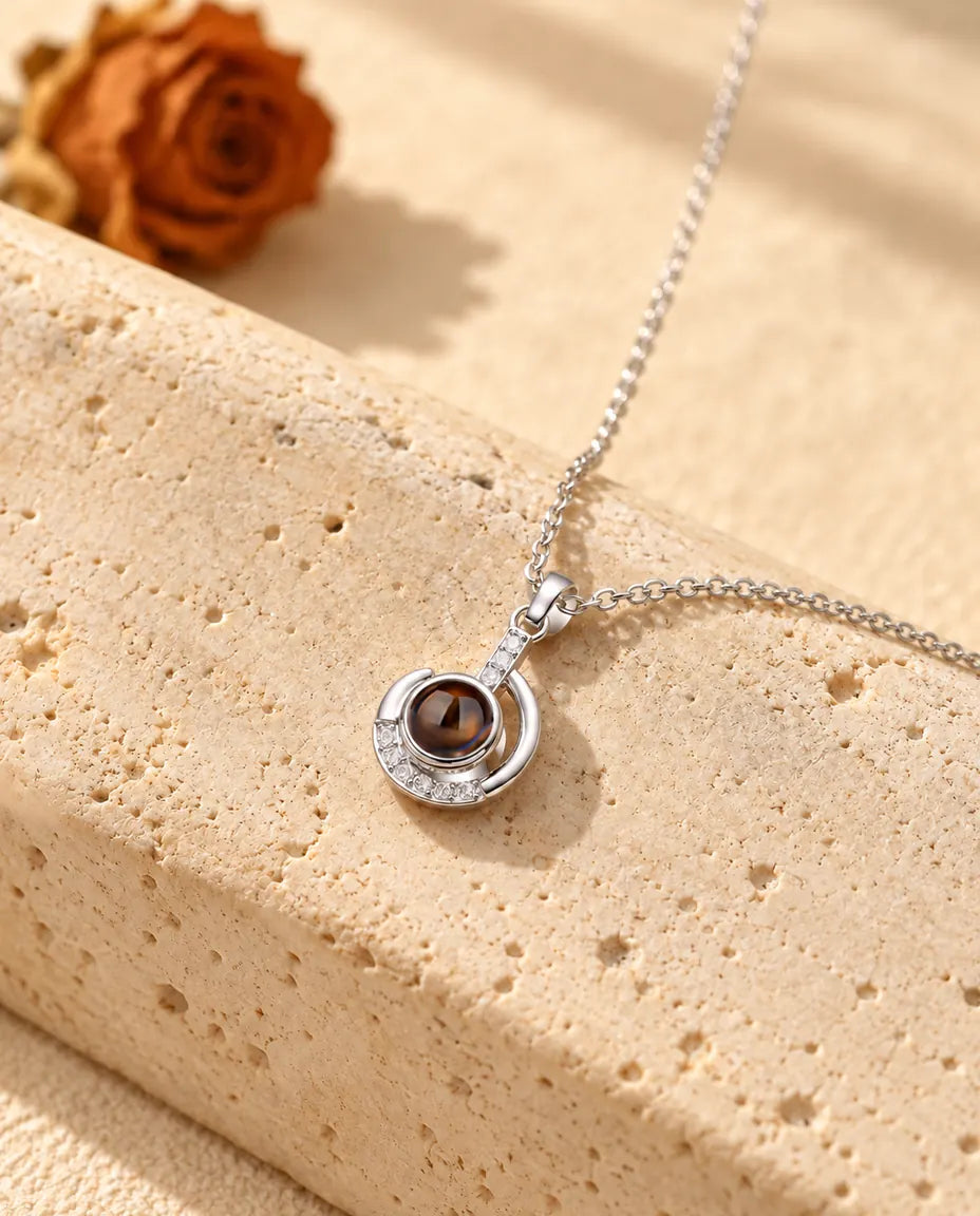 Silver tone crescent moon projection necklace hanging over travertine