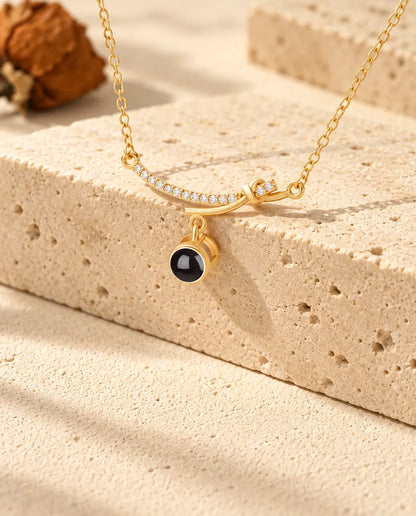 Personalized gold tone curved bar photo projection necklace draped over a travertine block