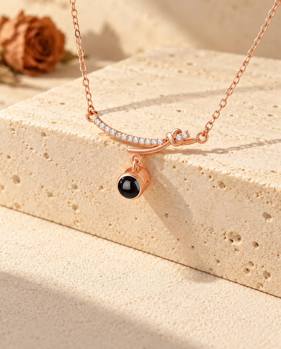 Rose gold tone curved bar necklace with its dangling projection stone over a travertine block