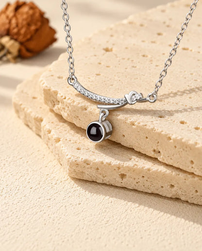 Silver tone curved bar projection necklace lying over the edge of a travertine slab