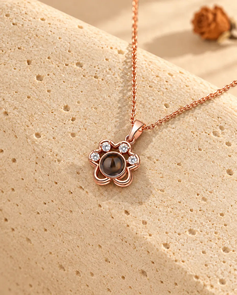 Rose gold tone paw print projection necklace hanging over travertine
