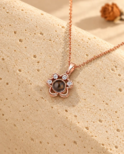 Rose gold tone paw print projection necklace hanging over travertine
