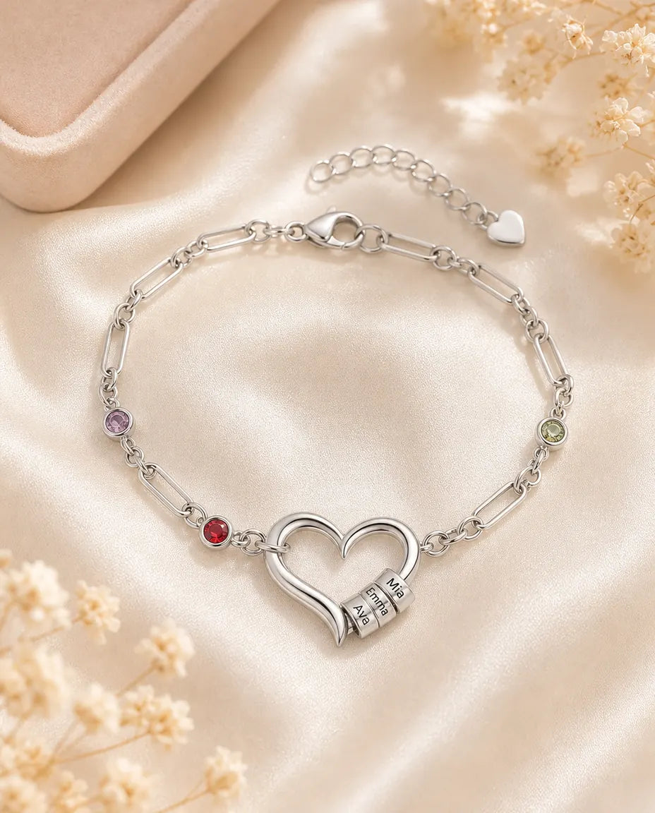 Personalized silver name bracelet with an open heart and birthstones, flat lay on cream silk