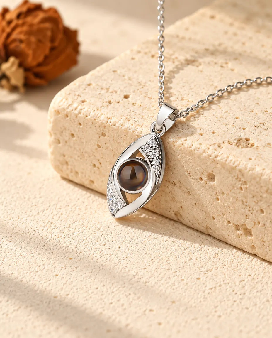 Personalized silver tone evil eye photo projection necklace lying over a travertine block