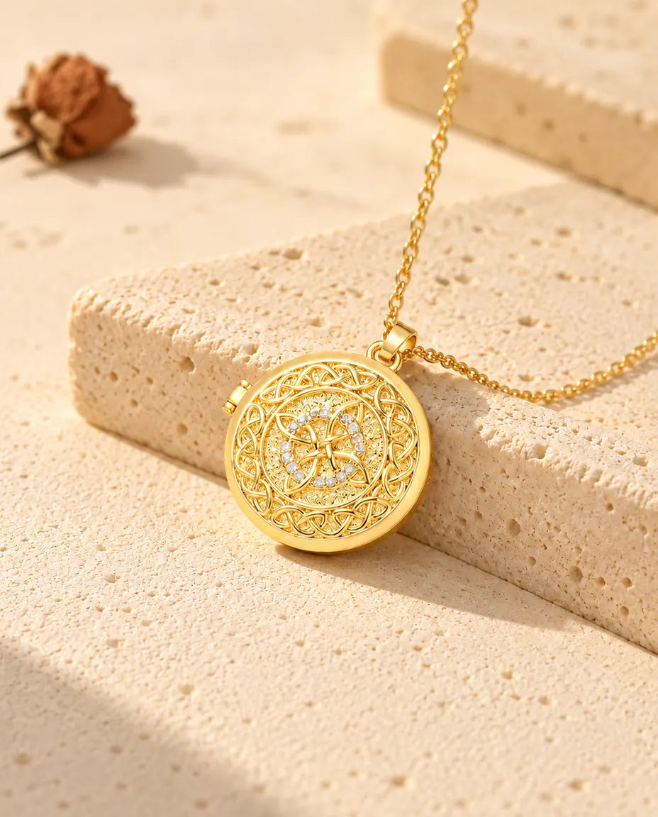 Gold tone four-loop Celtic knot photo locket necklace resting on a travertine block