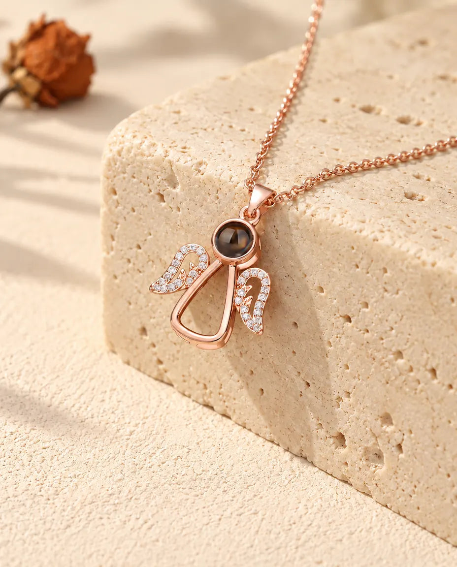 Rose gold tone angel projection necklace hanging over travertine