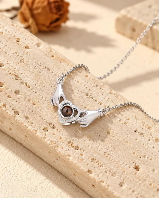 Personalized photo projection necklace in silver with two little hands holding a pave heart, resting on a travertine block