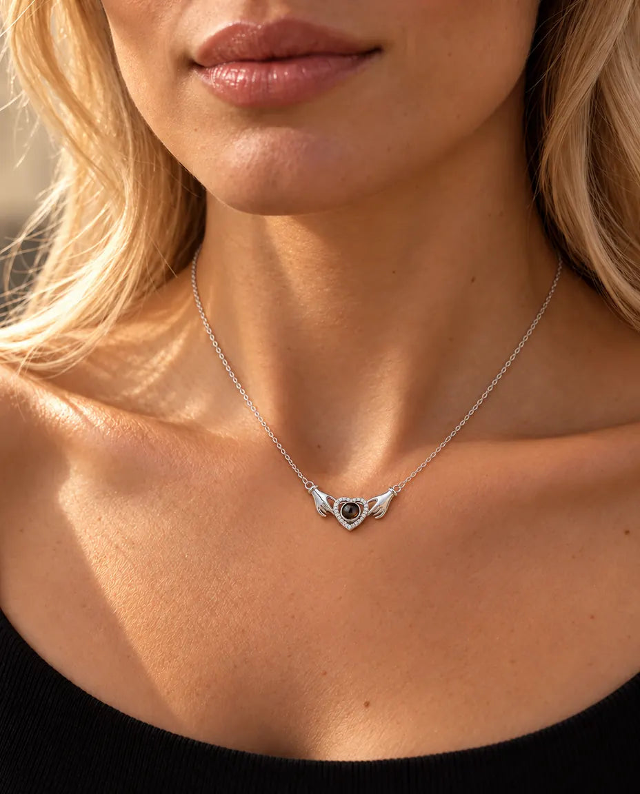 Woman in a black knit top wearing the silver hands holding heart photo projection necklace