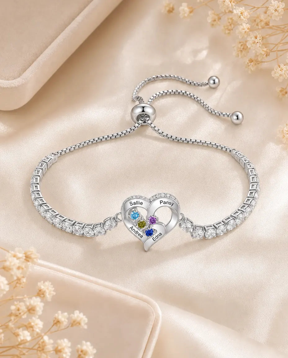 Personalized heart tennis bracelet with engraved names and birthstones, flat lay on cream silk