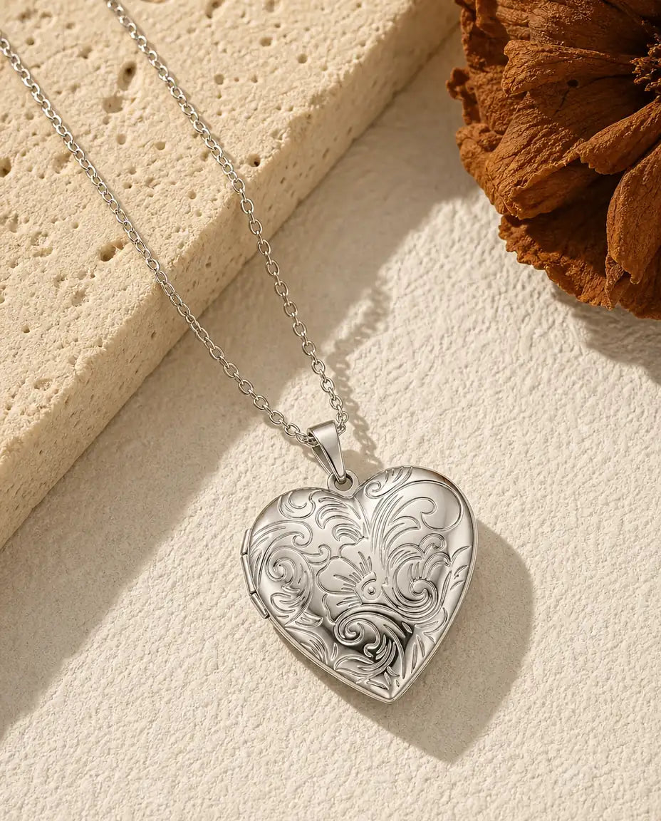 Personalized silver heart photo locket necklace with engraved floral front in warm flat-lay scene