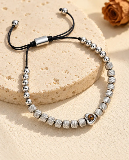 Personalized heart photo projection beaded bracelet in silver tone with textured barrel beads, on a travertine slab