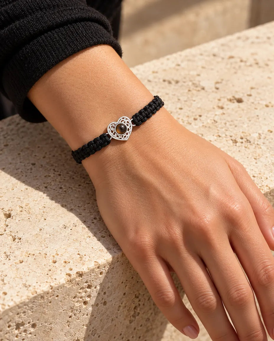 Woman wearing the black braided cord bracelet with a silver tone heart charm on her wrist in warm sunlight