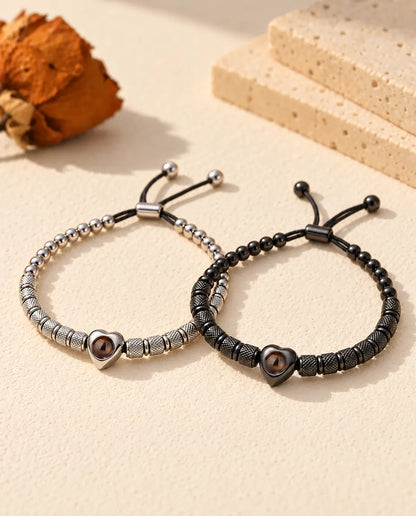 Personalized couples photo projection bracelets, a matching set of two heart bead bracelets in silver tone and black on cream plaster