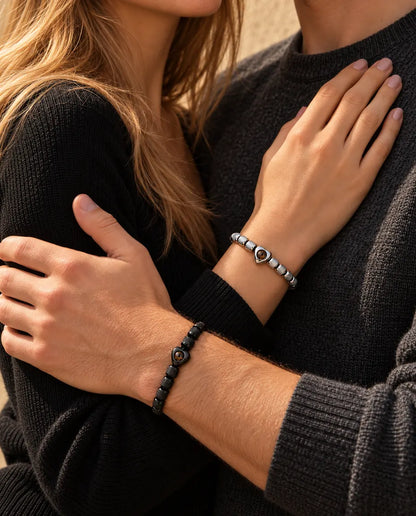 Couple in an embrace, she wears the silver tone heart projection bracelet and he wears the black one