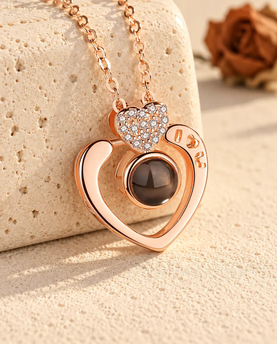 Personalized rose gold tone I love you open heart photo projection necklace resting on a travertine block