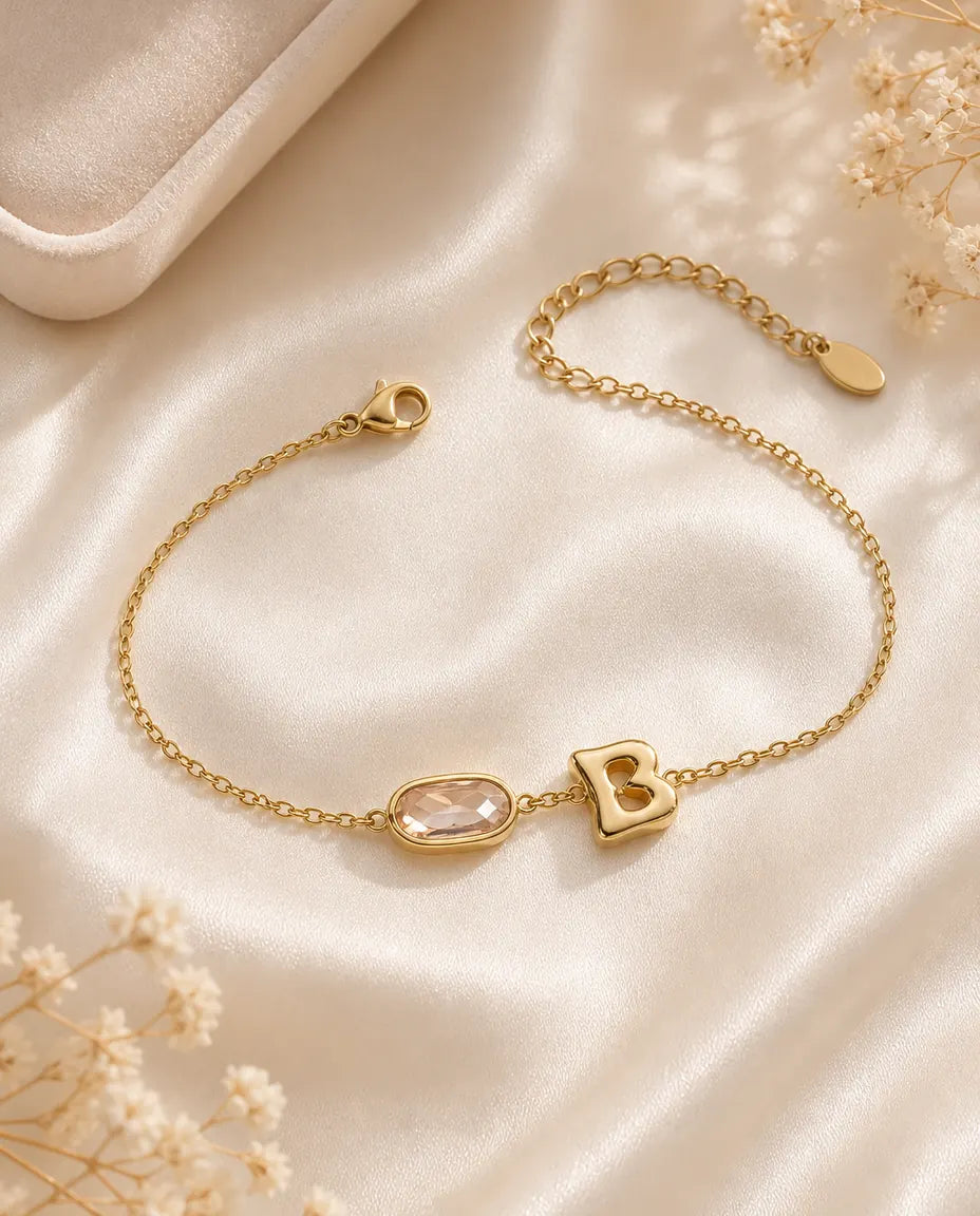 Personalized gold initial bracelet with an oval birthstone, flat lay on cream silk