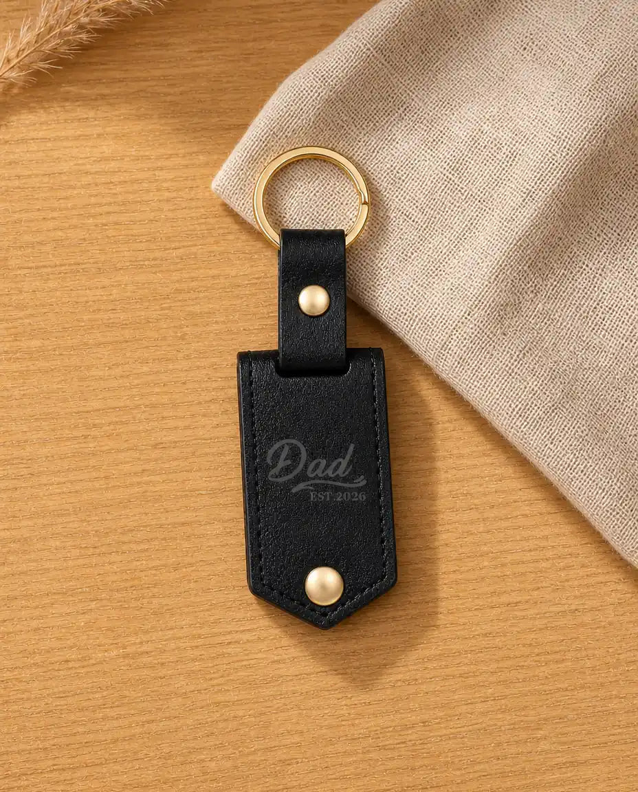 Personalized black leather photo keychain engraved with Dad Est. 2026 on a warm wood table