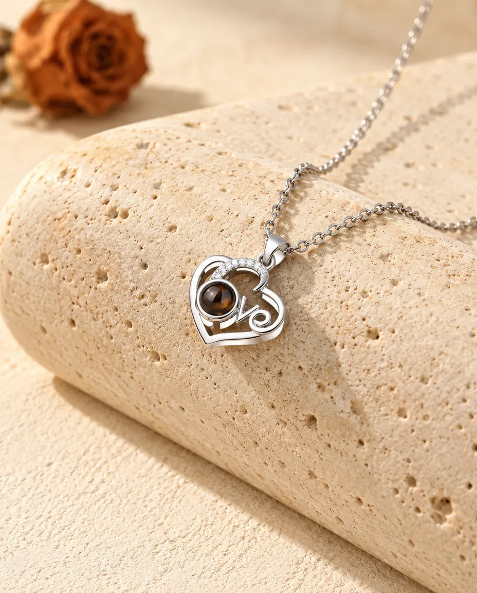 Personalized Love heart photo projection necklace in silver tone with a cubic zirconia arc, resting on a travertine block