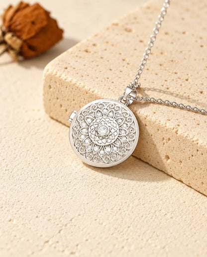 Personalized mandala flower photo locket necklace in silver tone with cubic zirconia petals, resting on a travertine block