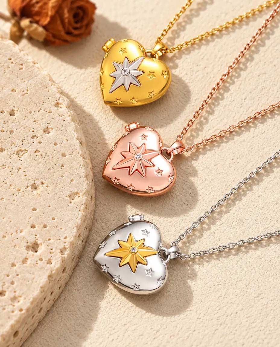 Gold tone, rose gold tone and silver tone north star heart photo lockets stacked beside a travertine slab