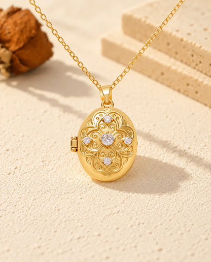 Front view of the gold tone oval locket showing the scrollwork flower, five stones and side hinge