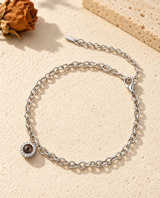 Personalized photo projection bracelet in silver tone with a tiny pave circle charm on a fine chain, lying on cream plaster