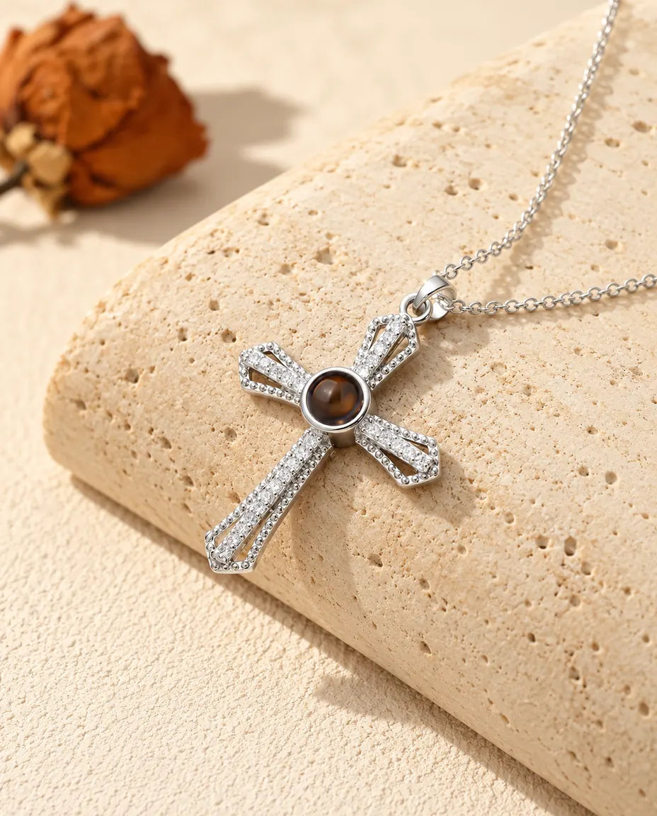 Personalized pave cross photo projection necklace in silver tone with a brown stone at the center, on a travertine block