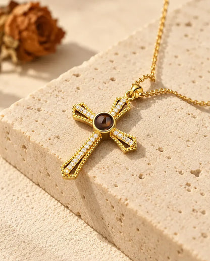 Gold tone open frame cross with a row of cubic zirconia resting on a travertine block