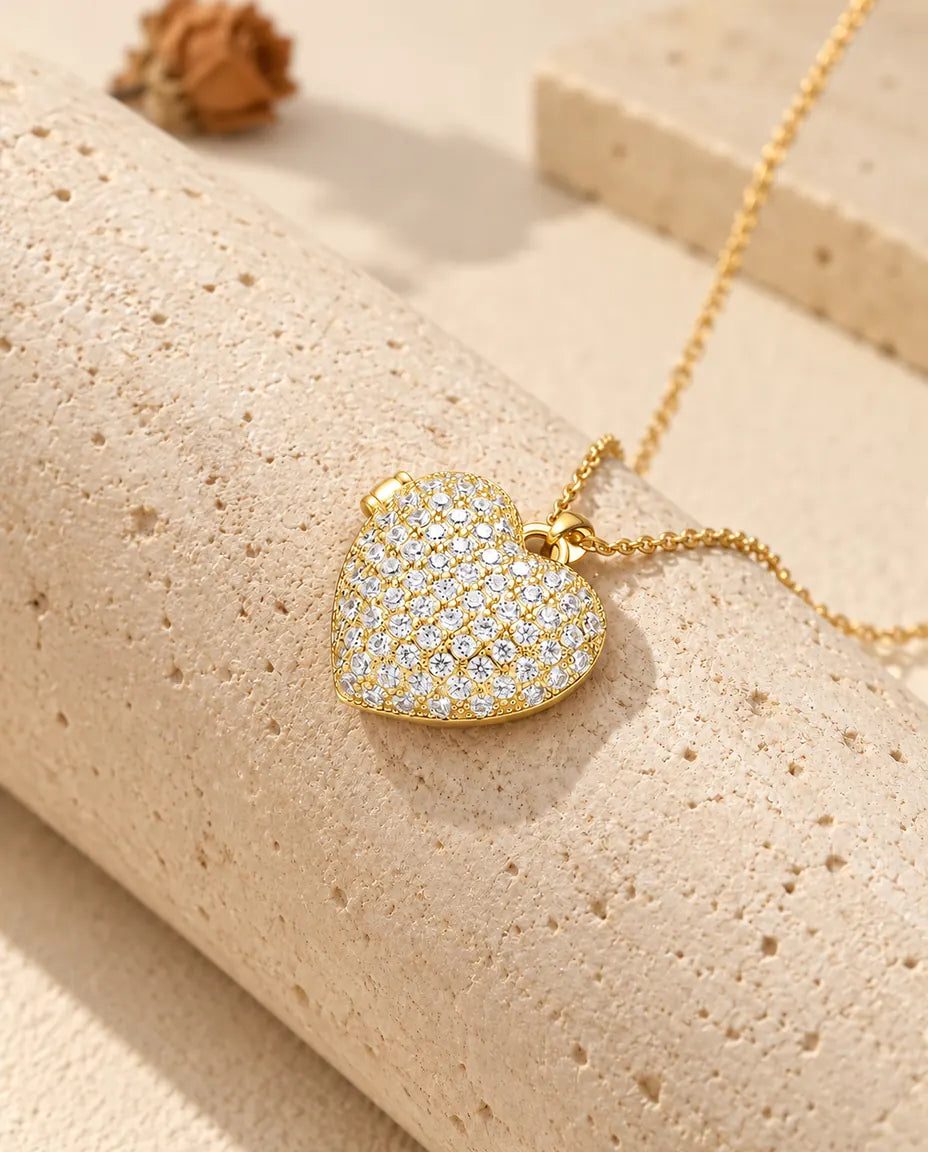 Gold tone pave heart photo locket necklace resting on a travertine block