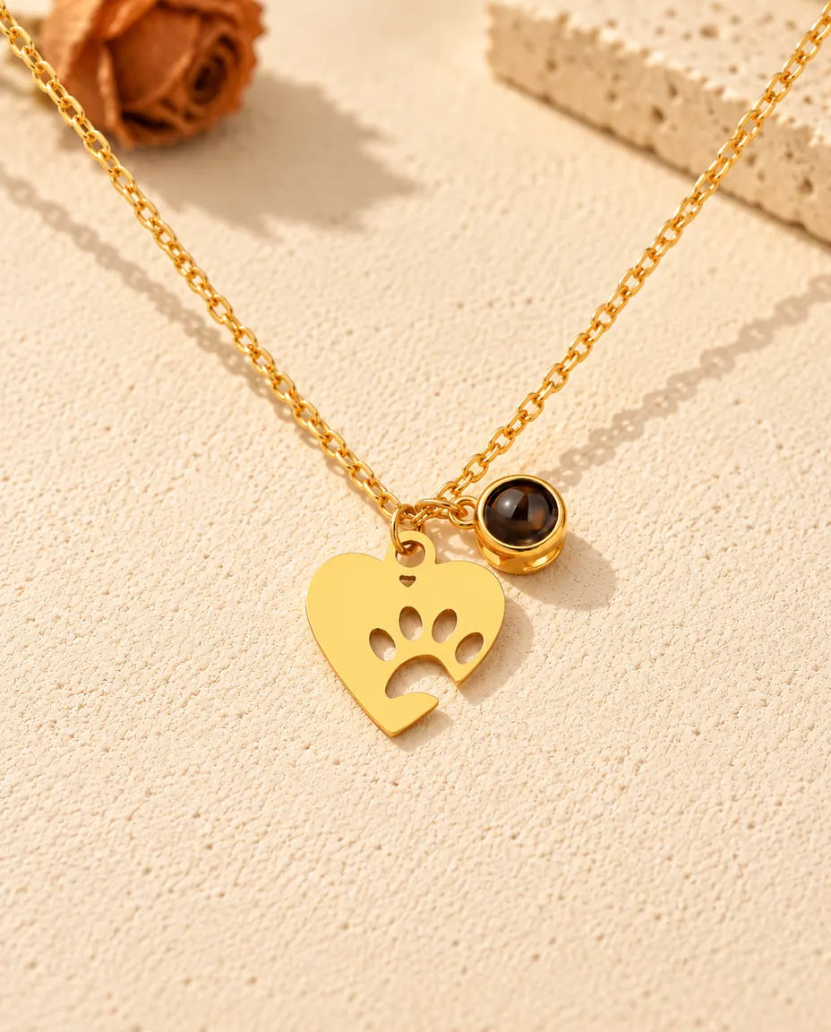 Front view of the gold tone paw print heart necklace with its projection stone charm