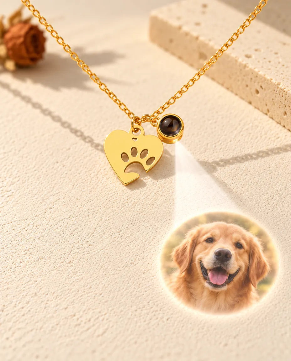 Light shining through the tiny brown stone of the gold tone paw heart necklace projects a photo of a golden retriever